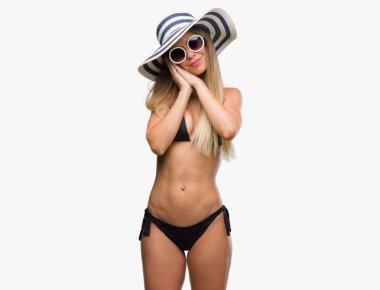 Bikini, güneş gözlüğü ve uyku yorgun hayal ve ile gülümseyen gözleri kapalı iken ellerle birlikte poz şapka giyen güzel genç kadın.