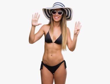 Bikini, güneş gözlüğü ve gösterilen ve parmakları ile işaret şapka giyen güzel genç kadın numara 9 kendinden emin ve mutlu gülümseyerek süre.