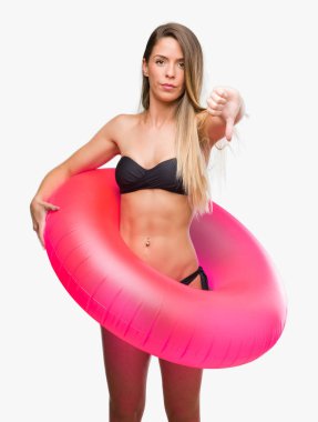 Kızgın yüz, eksi işareti aşağı antipati başparmak ile gösterilen, ret kavramı ile pembe float tutan Bikini güzel genç kadın