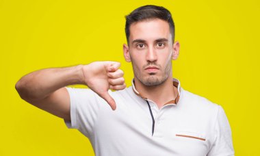 Handsome young casual man wearing white t-shirt with angry face, negative sign showing dislike with thumbs down, rejection concept clipart