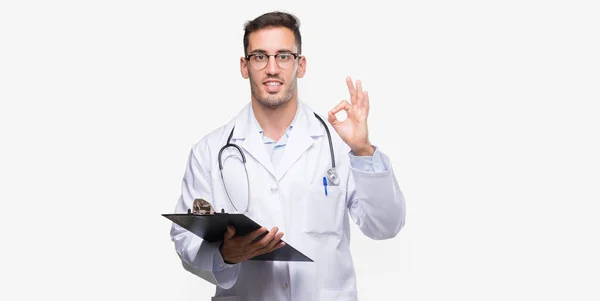 ハンサムな若い医者を抱きかかえた優秀なシンボルの指で サインをしているクリップボード — ストック写真