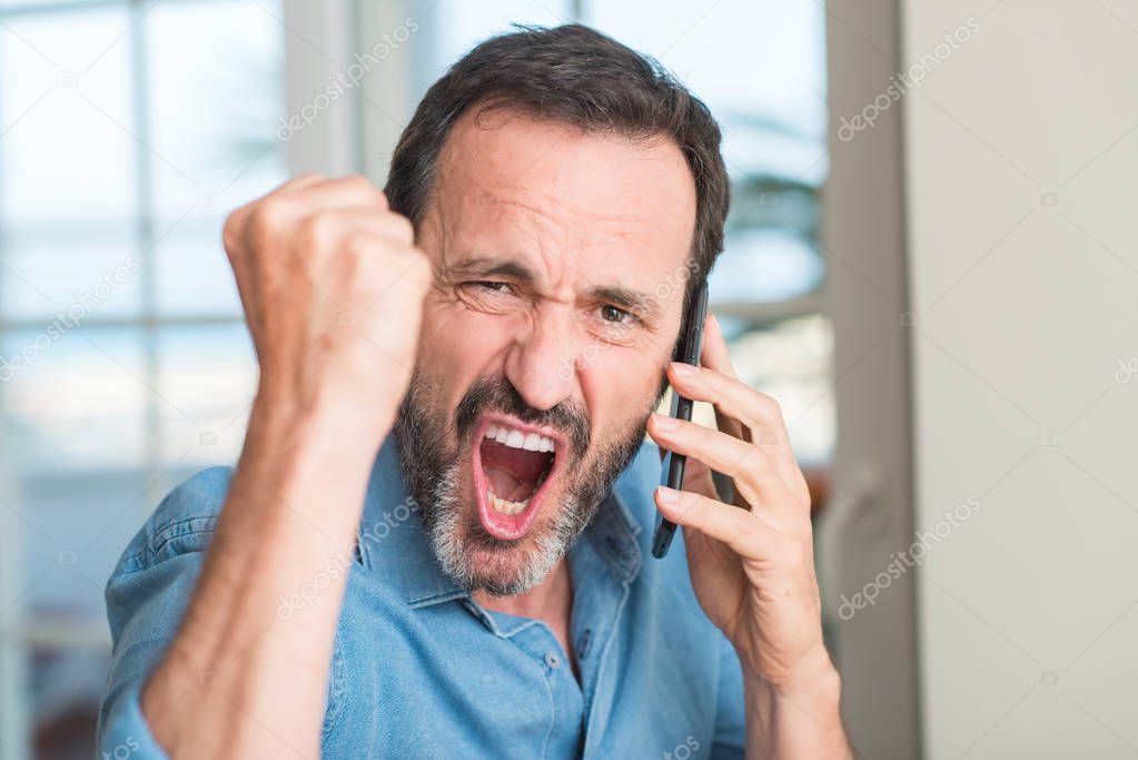 Middle age man using smartphone annoyed and frustrated shouting with anger, crazy and yelling with raised hand, anger concept