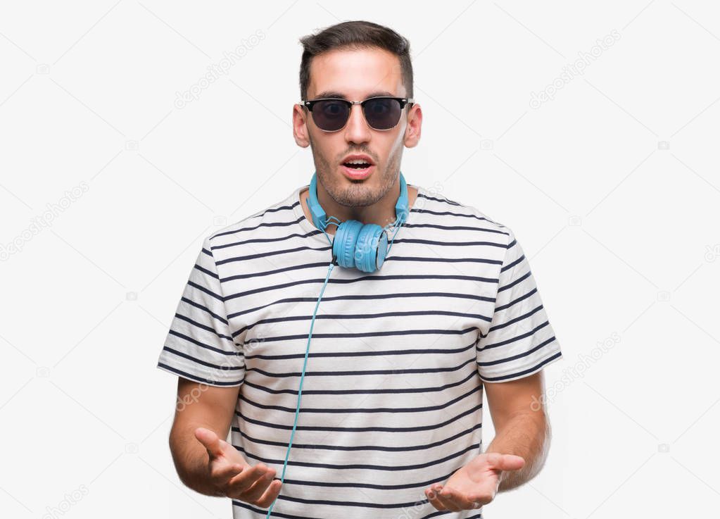 Handsome young man wearing headphones afraid and shocked with surprise expression, fear and excited face.