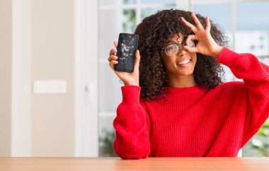 Kırık smartphone ile ok işareti ile el parmaklarının arasından seyir göze yapıyor gülümseyen mutlu yüz tutan Afrikalı-Amerikalı kadın