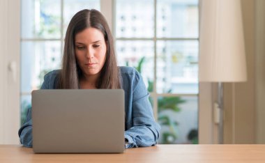 Genç kadın akıllı yüzünde ciddi düşünme emin bir ifade ile dizüstü evde kullanma