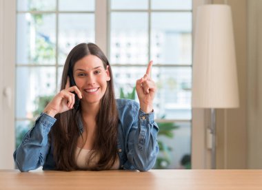 Bir fikir ya da soru işaret parmağı gülen yüz, bir numara ile Smartphone sürpriz kullanan genç kadın