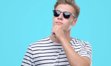 Sunglasess ciddi bir yüz düşünme hakkında soru, çok karışık fikir giyen genç yakışıklı sarışın adam