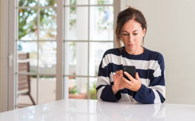 Acımak yüz düşünme ciddi kendine güvenen bir ifade ile akıllı telefon kullanan orta yaşlı kadın