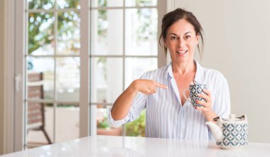 Orta yaşlı kadın kendini parmakla sürpriz yüz ile bir fincan çay ya da kahve içme