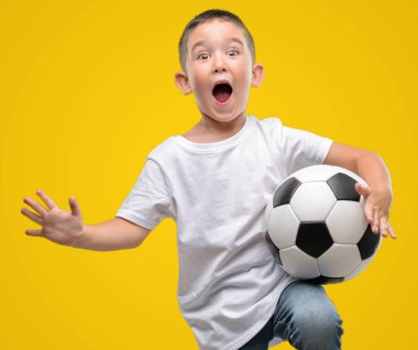 Kocaman bir gülümseme ile çığlık zaferini kutluyor ve ellerini kaldırdı futbol topu çok mutlu ve heyecanlı, kazanan ifade ile oynayan koyu saçlı küçük çocuk