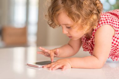 Güzel sarışın çocuk kullanarak ve evde smartphone ile oynamak.