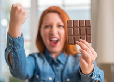 Evde rahatsız ve hayal kırıklığı ile öfke, çılgın ve yükseltilmiş eliyle diye bağıran öfke kavramı bağırarak bar çikolata tutan Kızıl saçlı kadın