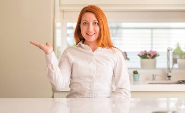 Kızıl saçlı kadın neşeli sunulması ve kameraya bakarak avucunun ile işaret gülümseyen mutfak at.