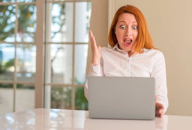 Bilgisayar dizüstü evde çok mutlu ve heyecanlı kullanan Kızıl saçlı kadın, kocaman bir gülümseme ile çığlık ve ellerini kaldırdı zaferini kutluyor kazanan ifade