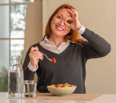Mutlu yüz el parmaklarının arasından seyir göz üzerinde ok işaretiyle yapıyor gülümseyen ile meyve tabağı, kivi ve çilek evde yemek Kızıl saçlı kadın