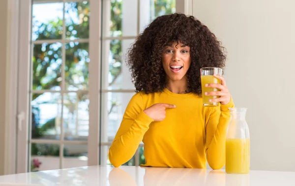 자신에 놀라운 가리키는 손가락으로 집에서 주스를 마시는 아프리카계 미국인 — 스톡 사진