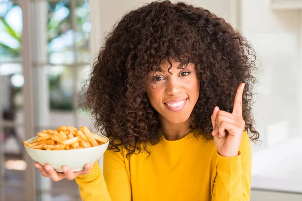 家でポテトチップスとプレートを保持しているアフリカ系アメリカ人の女性を幸せな顔で ナンバーワンのアイデアや質問ポインティング指で驚かせた — ストック写真