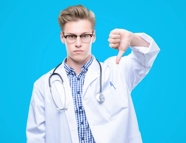 Young handsome blond doctor with angry face, negative sign showing dislike with thumbs down, rejection concept