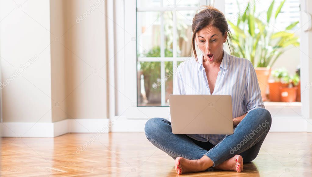 Middle aged woman using laptop at home scared in shock with a surprise face, afraid and excited with fear expression