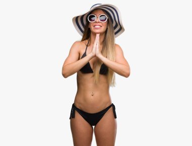 Bikini, güneş gözlüğü ve yalvarıyor ve umut ifade yüzünde çok duygusal ve endişe ile birlikte elleriyle dua şapka giyen güzel genç kadın. Bağışlanmak. Din kavramı.