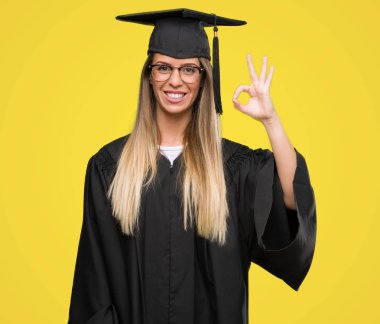 Gözlük ve parmak, mükemmel sembolü ile ok işareti yapıyor mezuniyet elbise giyen güzel genç kadın