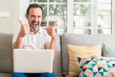 Ok işareti, başparmak ile parmak, mükemmel işareti yapıyor kocaman bir gülümseme ile kanepe mutlu dizüstü bilgisayar kullanan orta yaş adam