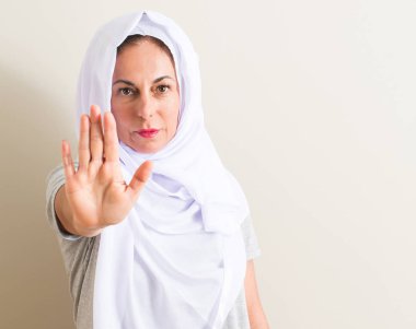 Orta yaş Arap kadın ile beyaz hijab giyen dur işareti ile ciddi ve kendine güvenen ifade, savunma hareketi yaparken el açmak
