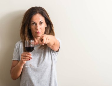 Orta yaş kadın içme kırmızı şarap bir bardak kamera ve size parmak ile işaret, el işareti, pozitif ve kendinden emin bir jest ön