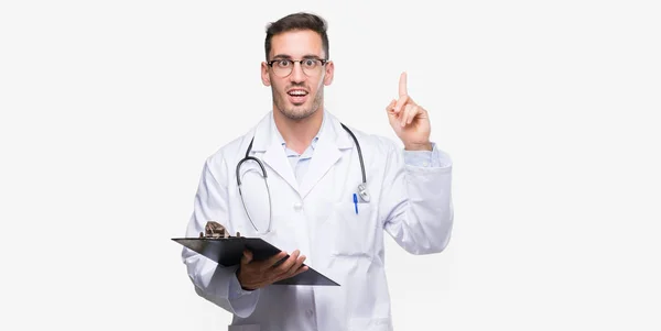 Handsome Young Doctor Man Holding Clipboard Surprised Idea Question Pointing — Stock Photo, Image
