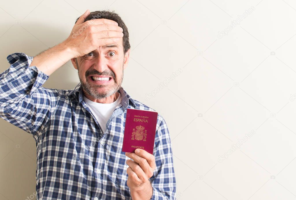 Senior man holding spanish passport stressed with hand on head, shocked with shame and surprise face, angry and frustrated. Fear and upset for mistake.