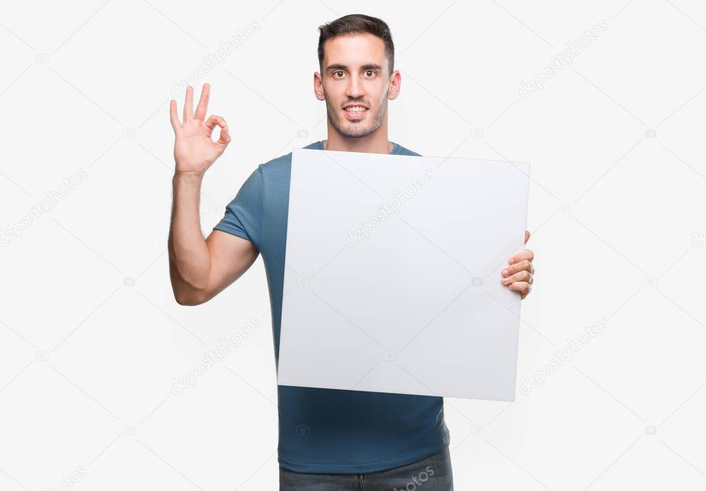 Handsome young man holding advertising banner doing ok sign with fingers, excellent symbol