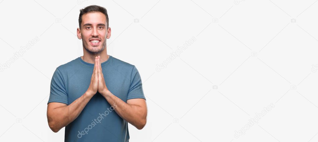 Handsome young casual man praying with hands together asking for forgiveness smiling confident.
