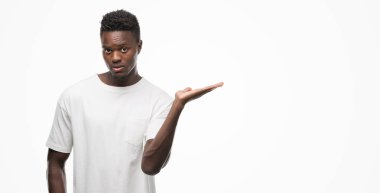Neşeli sunulması ve kameraya bakarak avucunun ile işaret gülümseyen beyaz t-shirt giyen genç Afro-Amerikan adam.