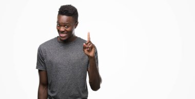 Gösterilen ve kendinden emin ve mutlu gülümseyen bir parmak ile işaret eden oktan yukarı gri t-shirt giyen genç Afro-Amerikan adam.