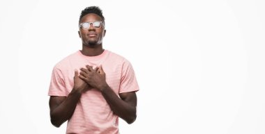 Afro-Amerikan delikanlı ile gülümseyen pembe t-shirt giyen kapalı gözler ve yüzünde minnettar jest ile göğüs üzerinde eller. Sağlık kavramı.