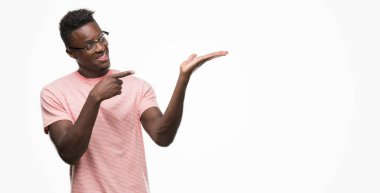 Hayret ve el ile sunulması ve parmak ile işaret ederken kameraya gülümseyen pembe t-shirt giyen genç Afro-Amerikan adam.