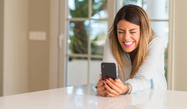 Young woman smiling happy using smartphone, holding mobile phone looking at home