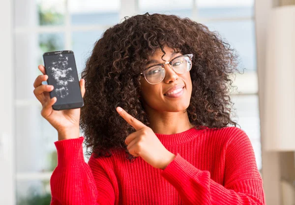 African american woman holding broken smartphone very happy pointing with hand and finger to the side