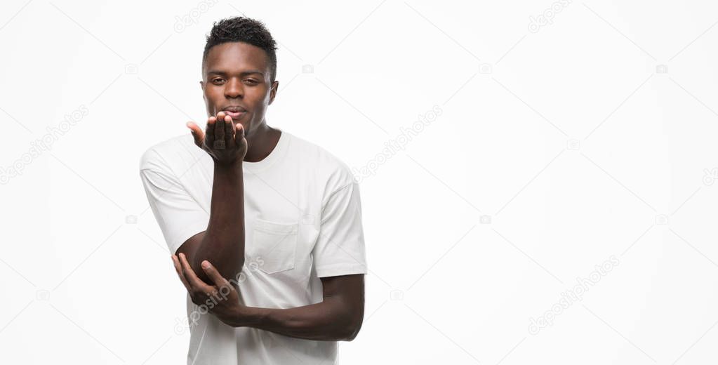 Young african american man wearing white t-shirt looking at the camera blowing a kiss with hand on air being lovely and sexy. Love expression.