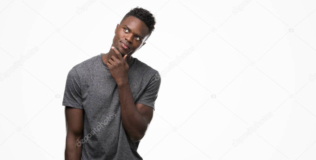 Young african american man wearing grey t-shirt with hand on chin thinking about question, pensive expression. Smiling with thoughtful face. Doubt concept.