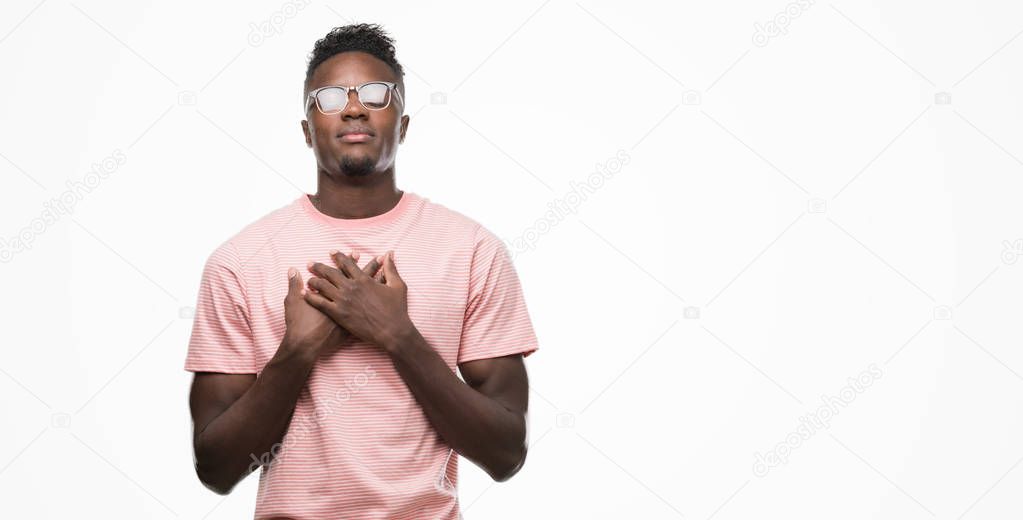 Young african american man wearing pink t-shirt smiling with hands on chest with closed eyes and grateful gesture on face. Health concept.