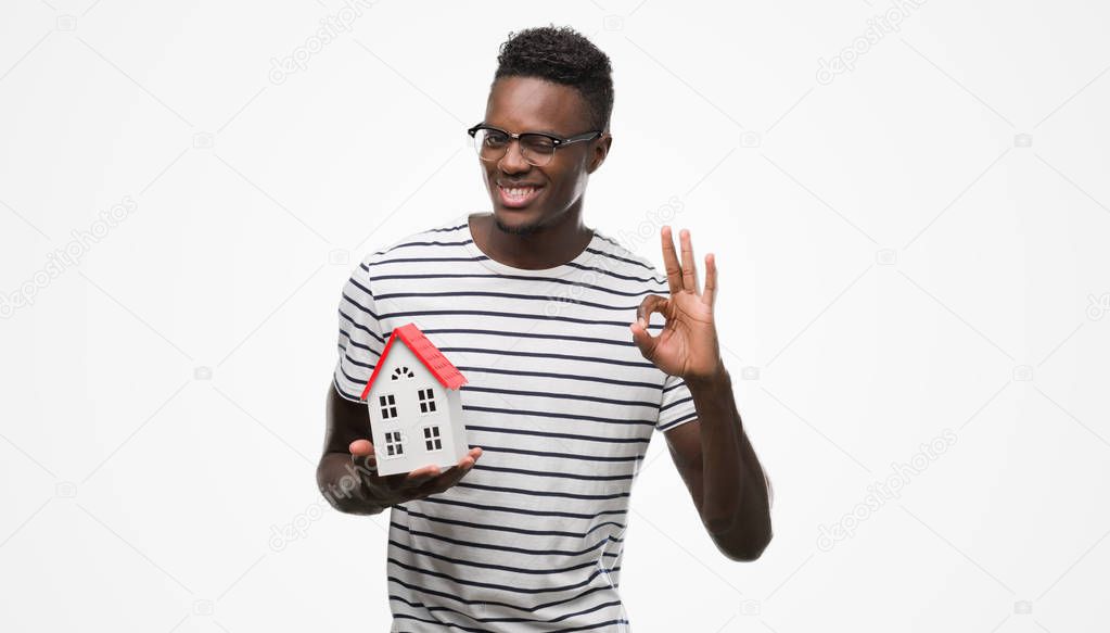 Young african american man holding house doing ok sign with fingers, excellent symbol