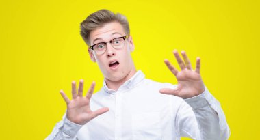 Şokta bağırarak genç yakışıklı sarışın adam korkuyor ve korku ifade dur hareketi el ile ile çok korkmuş. Panik kavramı.