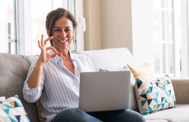 Orta yaşlı kadın parmakları, mükemmel sembolü olan ok işareti yapıyor kanepe dizüstü bilgisayar kullanarak