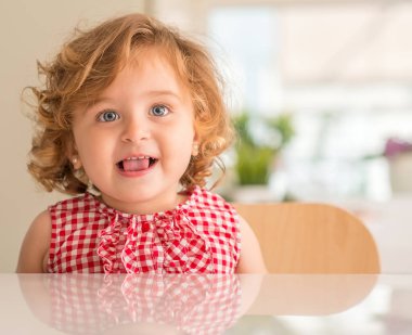 Dilini çıkarmış evde gülümseyen mavi gözlü güzel sarışın çocuğun.