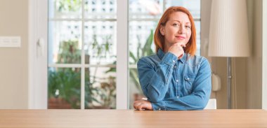 Kızıl saçlı kadın evde emin çapraz kollar ve çeneme kaldırdı el ile gülümseme ile kameraya bakıyor. Pozitif düşünce.