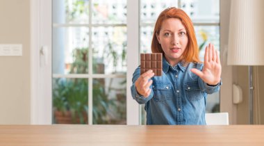 Evde açık eliyle dur işareti ile ciddi ve kendine güvenen ifade, savunma jest yapıyor çikolata bar tutan Kızıl saçlı kadın