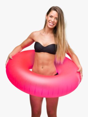 Güzel genç kadın ayakta ve diş gösterilen kendine güvenen bir gülümsemeyle gülümseyerek mutlu bir yüz ile pembe float tutan bikini