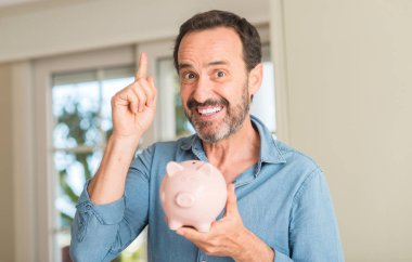 Orta yaş erkek kumbara bir fikirle sürpriz tasarruf ya da gülen yüz, bir numara ile işaret parmağı soru