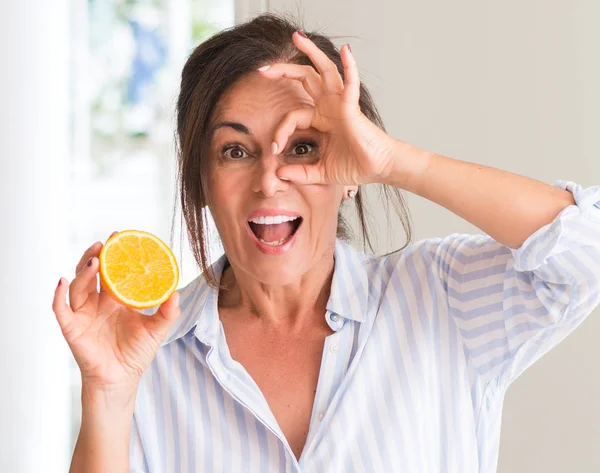 オレンジ色の果物を保持して指を通して見る目に手で サインをして笑っている幸せそうな顔で中年の女性 — ストック写真